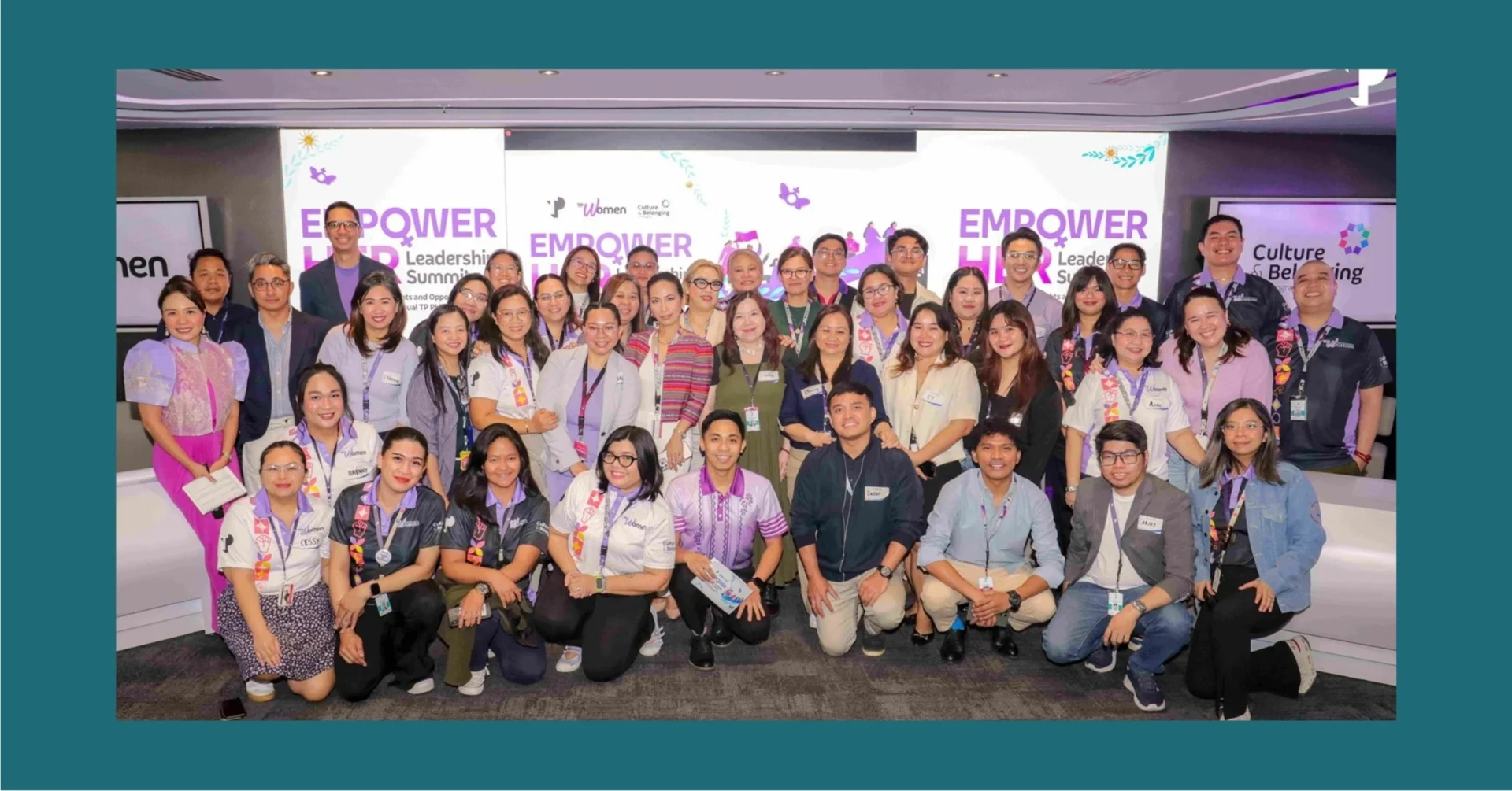 Diverse group of attendees posing for a photo at the Empower Her Leadership Summit with a banner backdrop reading Empower Her.